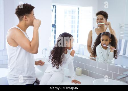 Père et fille multiracial se brossant tout en regardant le miroir de réflexion dans la salle de bains Banque D'Images