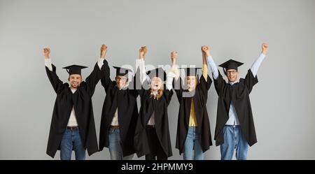 Portrait d'un groupe heureux et réussi de diplômés multiraciaux debout dans la rangée tenant les mains. Banque D'Images