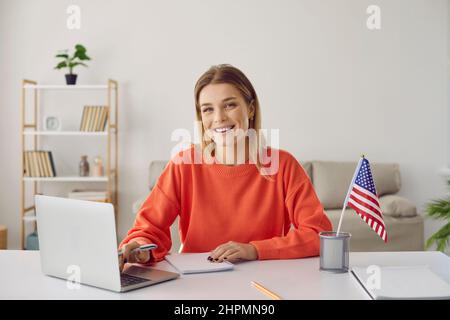 Portrait d'une jeune femme heureuse avec drapeau américain apprenant l'anglais américain en ligne à partir de la maison à l'aide d'un ordinateur portable. Banque D'Images