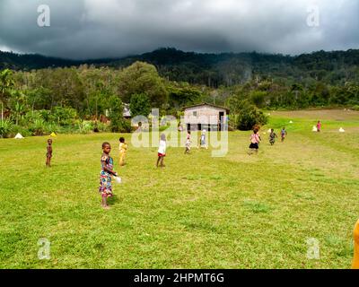 Jeunes enfants jouant au football dans la province des Highlands de l'est de la PNG, haute altitude dans le territoire de culture du café, forêt tropicale de montagne en arrière-plan Banque D'Images