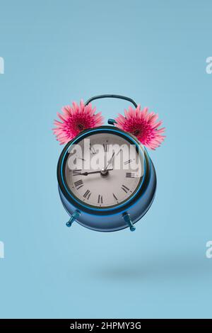 Réveil rétro Vintage avec de belles fleurs de gerbera fraîches volées dans l'air isolé sur fond bleu pastel. Période créative du printemps ou de l'été c Banque D'Images