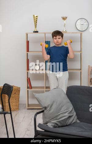 Un jeune garçon s'exerce avec des haltères dans sa chambre. Banque D'Images