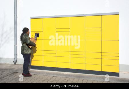 Station de colis de poste automatisée avec femme à l'écran de commande tenant le téléphone mobile et le paquet Banque D'Images