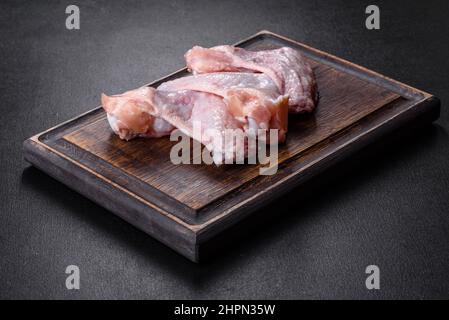 Viande crue. Les ailes de poulet se trouvent sur une planche en bois avec des légumes et des épices sur fond noir Banque D'Images
