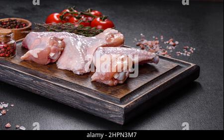 Viande crue. Les ailes de poulet se trouvent sur une planche en bois avec des légumes et des épices sur fond noir Banque D'Images