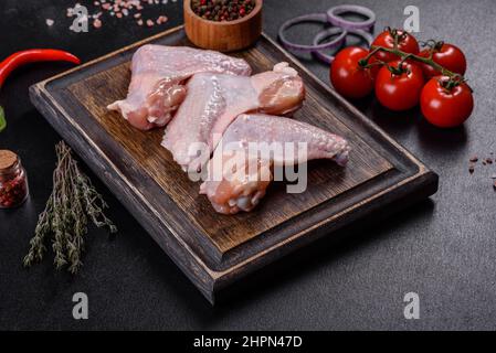 Viande crue. Les ailes de poulet se trouvent sur une planche en bois avec des légumes et des épices sur fond noir Banque D'Images