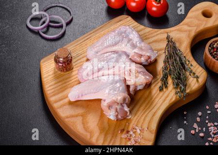 Viande crue. Les ailes de poulet se trouvent sur une planche en bois avec des légumes et des épices sur fond noir Banque D'Images