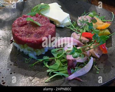 Tartare de viande crue avec des légumes verts et du riz sur une composition de plat noir Banque D'Images