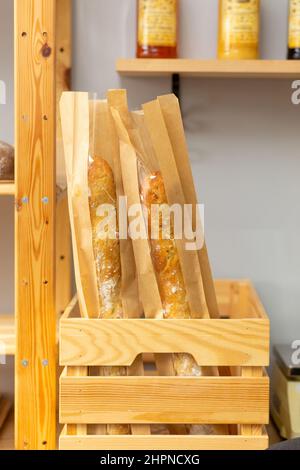 Deux baguettes fraîches dans un paquet sont dans une boîte en bois dans une épicerie ou un café. Banque D'Images