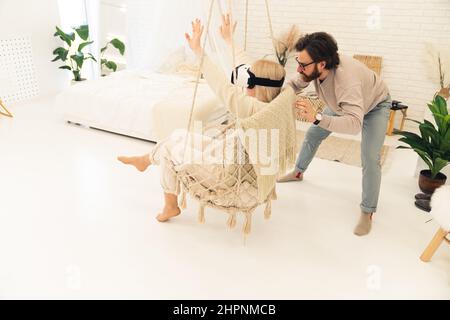 Jeune entrepreneur caucasien montrant sa fiancée aux cheveux blonds la technologie derrière les lunettes VR dans leur appartement moderne. Photo de haute qualité Banque D'Images