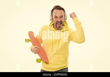 homme heureux écouter de la musique dans les écouteurs tenir penny skateboard isolé sur blanc, skateboard hobby. Banque D'Images