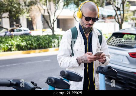 Un homme chauve équipé d'un casque utilise une application pour monter à bord d'un scooter de système public Banque D'Images