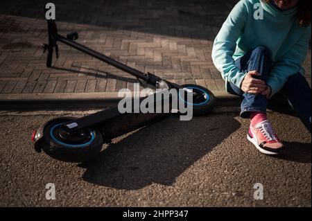 Une femme de race blanche est tombée d'un scooter électrique et a blessé sa jambe.Souffrant de douleur. Banque D'Images