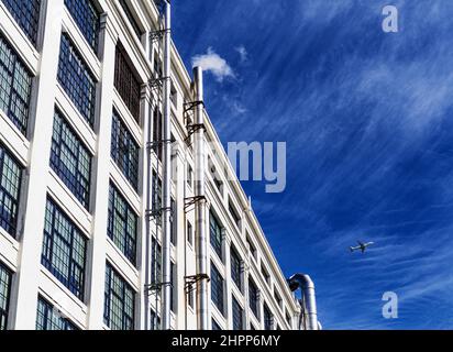 Vue à angle bas de l'extérieur du bâtiment industriel commercial de plusieurs étages avec ciel bleu spectaculaire et image airplace à petit jet. Banque D'Images