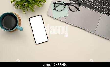 Vue de dessus, simple arrière-plan blanc d'espace de travail avec ordinateur portable, lunettes, notes adhésives, tasse à café, plante de décor et maquette d'écran blanc de smartphone Banque D'Images