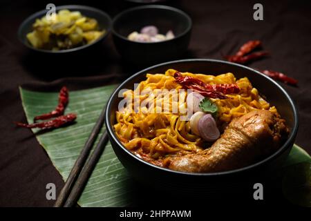 Cuisine traditionnelle du nord de la Thaïlande, Khao soi Kai, curry jaune crémeux et épicé avec pilon de poulet servi avec un plat d'accompagnement de légumes. Banque D'Images