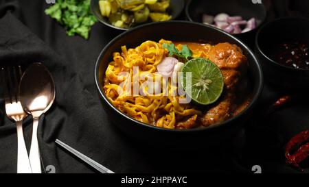 Célèbre et unique cuisine du nord de la Thaïlande, Khao soi Kai, nouilles aux œufs dans le curry jaune épicé avec des pilons de poulet vue de dessus citron vert, échalotes et coriandre Banque D'Images