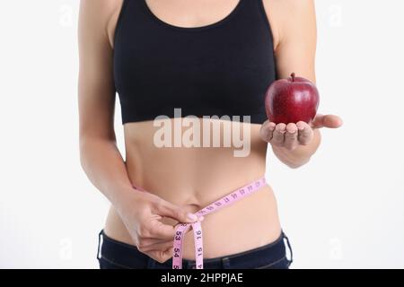 Une fille mince montre la pomme et le ruban de mesure autour de la taille Banque D'Images