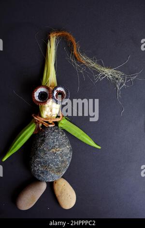 Drôle de visage mis en place de la nourriture, produit agricole de jardin sur le toit, petit maïs, fleur de citrouille, soie de maïs, fruit d'okra, cailloux et yeux crochet de Banque D'Images