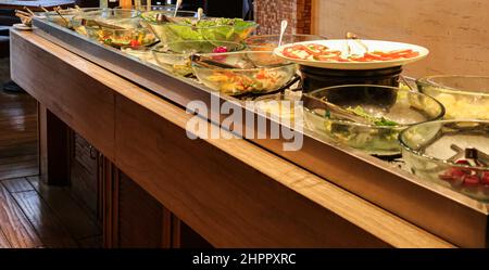 Laitue et fruits dans des bols en verre sur glace et salade de capres sur plaque blanche avec pinces en acier inoxydable au buffet froid de salades Banque D'Images