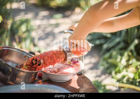 Préparer du jus de tomate maison en appuyant à la main avec une vis les enfants aident à tourner la poignée le jus sort de la pulpe à travers un tamis le Banque D'Images