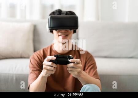 Concept de technologie Un homme mettant sur un casque de réalité virtuelle et appuyant sur un jeu de console noir tout en étant assis sur le sol. Banque D'Images