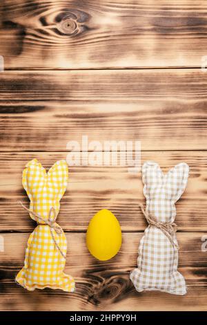 Carte postale de Pâques pour les fêtes de fête, deux lapins carrés faits à la main de couleur marron, blanche et jaune avec foulard sur fond de bois, jaune Banque D'Images