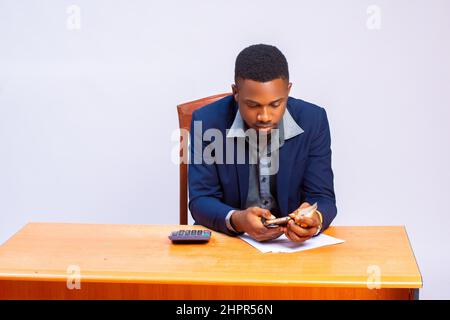 Le beau homme d'affaires africain calcule ses dépenses à l'aide d'une calculatrice Banque D'Images