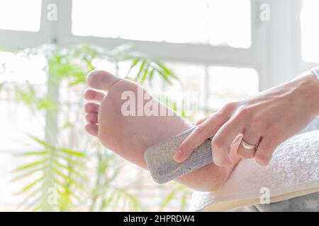mains d'une jeune femme utilisant une pierre ponce pour adoucir les calloses sur ses pieds. concept soins du corps, pédicure et réflexologie des pieds Banque D'Images