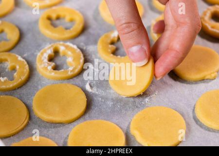 Gros plan les mains de la femme mettent des biscuits de sucre en forme d'anges sur le papier de cuisson prêt pour la Saint Valentin. Biscuits faits maison Banque D'Images