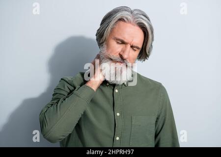 Portrait de l'homme attrayant fatigué gris-cheveux se touchant le cou se sentant mal isolé sur fond gris pastel couleur Banque D'Images