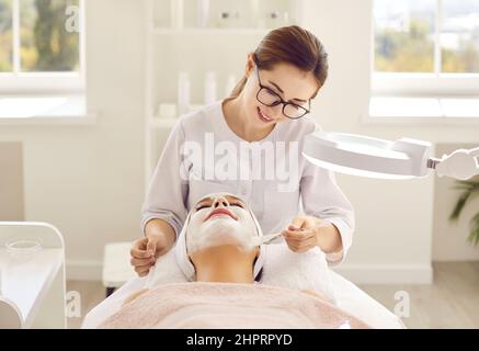 La cosmétologue professionnelle féminine applique un masque sur le visage du patient pour le soin de la peau du visage. Banque D'Images