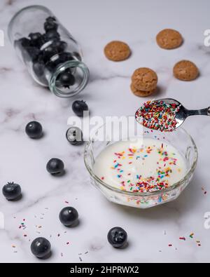 Le dessert préparé avec du yaourt blanc, des macarons, des bleuets et des saupoudriers arc-en-ciel couvre sur fond de marbre Banque D'Images