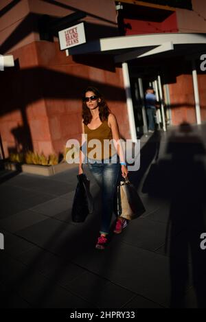 Une jeune femme attirante qui porte des sacs de shopping sort du centre commercial Banque D'Images