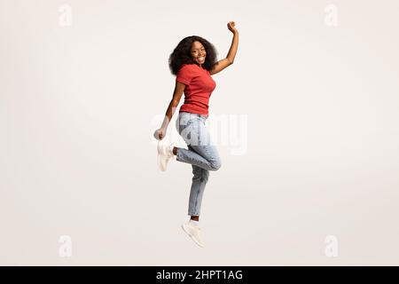 Une jeune femme noire insouciante qui saute dans l'air et regarde l'appareil photo Banque D'Images