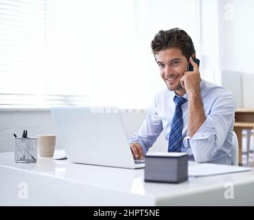 Bien sûr, nous pouvons le faire pour vous. Un jeune homme d'affaires parlant au téléphone tout en étant assis à son bureau. Banque D'Images