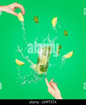 Femme soutien main Fly verre de délicieux cocktail Mojito avec lime et menthe avec des éclaboussures, ingrédients tombant à glassful. Concept de cuisine artistique d'été sur le plat Banque D'Images