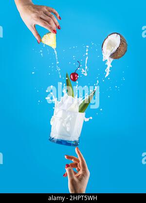 Femme mains soutien Fly verre de délicieux congelé Pina Colada traditionnel des Caraïbes cocktail avec splash, ingrédients tombant dans le verre. Arrière-plan bleu Banque D'Images