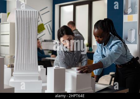 Les ingénieurs en architecture qui travaillent en équipe lisent les plans de construction sur une table avec un modèle d'échelle en mousse blanche des bâtiments. Équipe de deux architectes collègues travaillant en collaboration pour étudier les plans. Banque D'Images