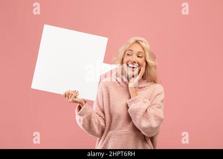 Une jeune femme surjoyeuse tenant et regardant la bulle de parole vide, posant sur fond de studio rose, mockup Banque D'Images