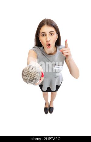 Vue en grand angle de la jeune fille émotive, journaliste femme tenant le microphone de journaliste isolé sur fond blanc de studio. Concept de médias sociaux Banque D'Images