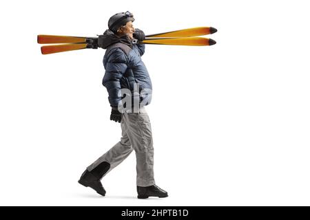 Photo pleine longueur d'un homme mature dans un équipement de ski marchant et portant des skiis sur son épaule Banque D'Images