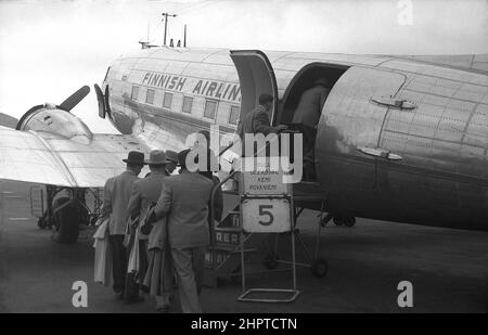 1940s, passagers historiques de sexe masculin, plusieurs portant des manteaux de pluie et des chapeaux, à bord d'un avion de compagnie aérienne finlandaise PROPELLER Douglas DC-3, à l'aéroport d'Helsinki, en Finlande. Banque D'Images