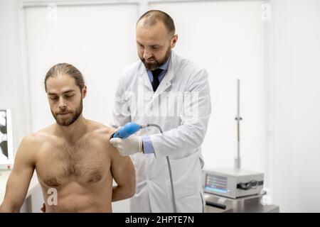 Le médecin applique un traitement par onde de choc sur l'épaule des hommes Banque D'Images