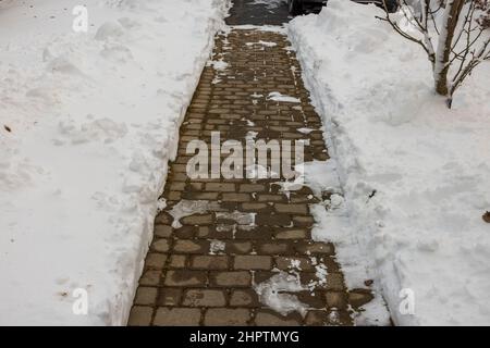 Magnifique vue sur le paysage naturel de la cour couverte de neige. Déneigements le long de la voie de passage dégagée en dalles de pavage grises. Suède. Banque D'Images