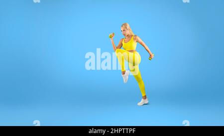 Jeune femme s'exerçant avec des haltères isolées sur fond bleu Banque D'Images