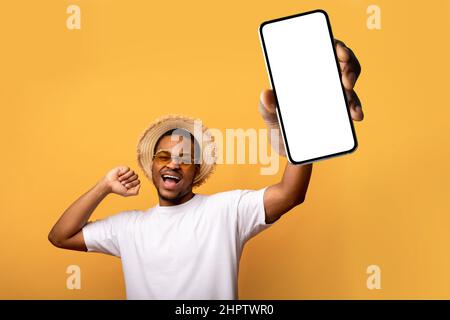 Beau homme noir en lunettes de soleil et chapeau de paille montrant smartphone avec maquette pour la conception d'application mobile ou de site Web Banque D'Images
