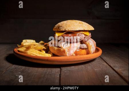 Hamburger de bœuf grillé de qualité supérieure avec bacon, fromage et frites. Délicieux hamburger américain sur fond de bois. Photographie de haute qualité Banque D'Images