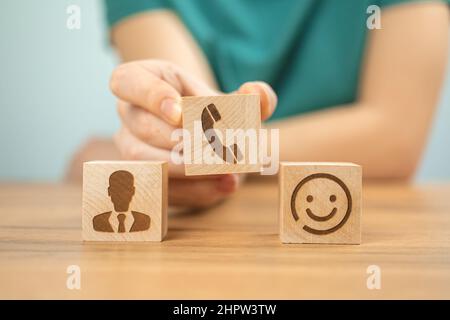 Client satisfait avec l'expérience du concept de service de centre d'appels. Assistance, service client et assistance. Cubes en bois avec des icônes et une main de jeune femme en offi Banque D'Images