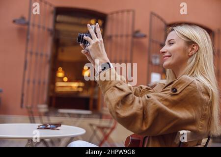 Vue latérale d'une femme prenant des photos avec un appareil photo rétro en étant assise à l'extérieur Banque D'Images